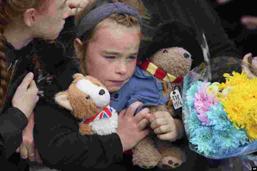 A young girl holds a Paddington bear and a Corgi dog stuffed toys while waiting to watch the Procession of Queen Elizabeth's coffin from the Palace of Holyroodhouse to St. Giles' Cathedral on the Royal Mile in Edinburgh, Sept. 12, 2022.