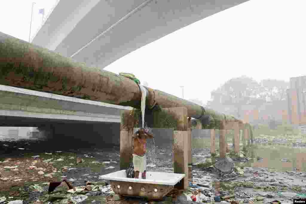 A man takes a bath under a leaking pipeline of water on a smoggy morning in New Delhi, India.