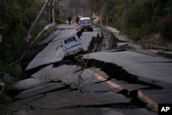 Bystanders look at damages somewhere near Noto town in the Noto peninsula facing the Sea of Japan, northwest of Tokyo, Tuesday, Jan. 2, 2024. (AP Photo/Hiro Komae)