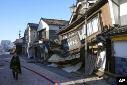 People walks past a collapsed houses following an earthquake in Wajima, Ishikawa prefecture, Japan Tuesday, Jan. 2, 2024. (Kyodo News via AP)