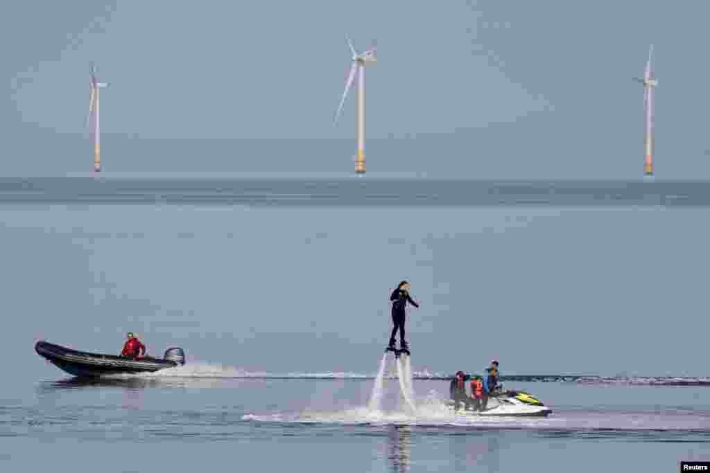 A speedboat passes a person using a flyboard near a wind farm on an unseasonably hot day in Herne Bay, Britain, Oct. 8, 2023.