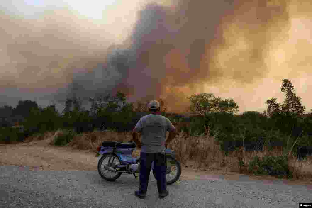 A local watches flames and smoke rising as a wildfire burns at the Dadia National Park in the region of Evros, Greece.