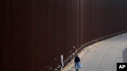 Una voluntaria camina a lo largo de un muro fronterizo mientras reparte toallitas húmedas para bebés a los migrantes que esperan solicitar asilo entre dos muros fronterizos el jueves 11 de mayo de 2023 en San Diego.