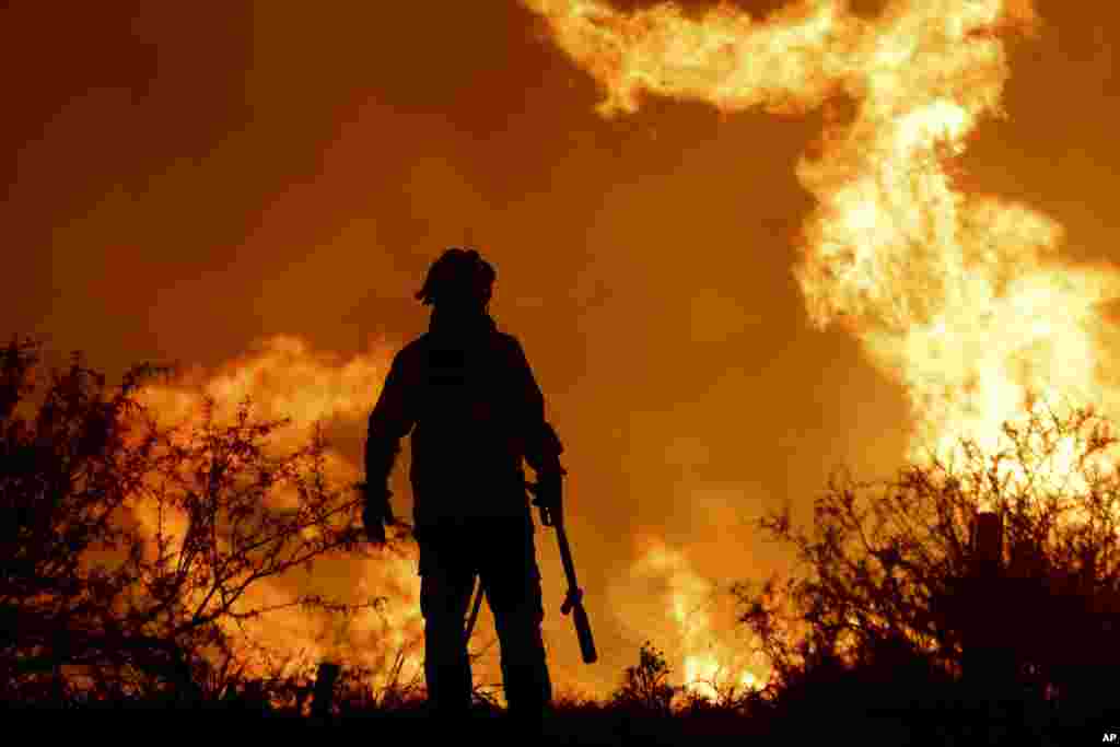A firefighter is silhouetted by the flames of a forest fire on the outskirts of Villa Carlos Paz, Argentina, Oct. 10, 2023.
