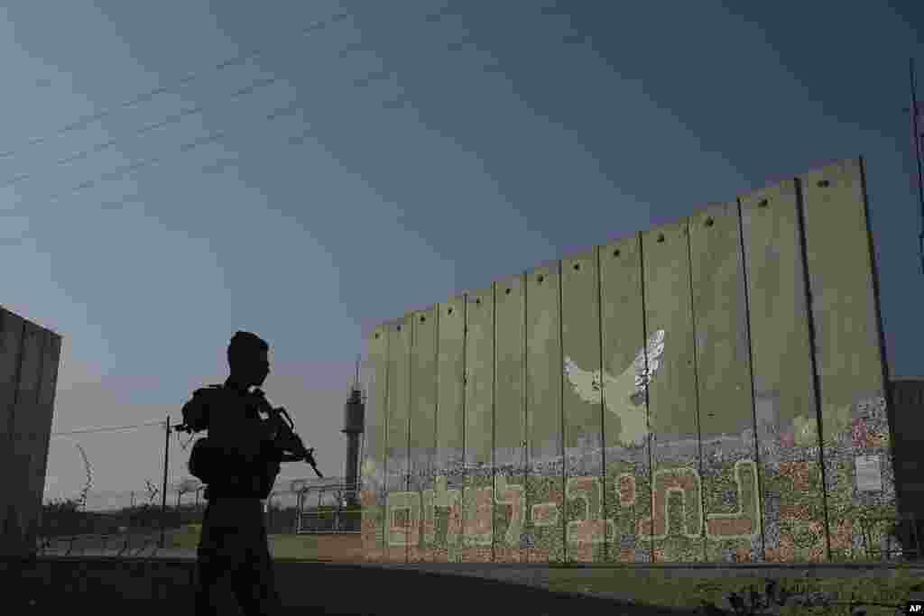 A member of Israeli forces stands next to a security wall with Hebrew writing reading "Path to Peace" at the Kibbutz Netiv Haasara near the border with Gaza Strip, Israel.