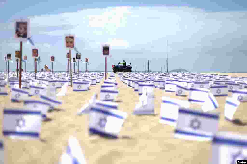 A policeman passes by, as Israel flags and pictures symbolizing victims are placed in Copacabana beach by NGO Rio de Paz, one month on from the October 7th attack by the Palestinian Islamist group Hamas, in Rio de Janeiro, Brazil.