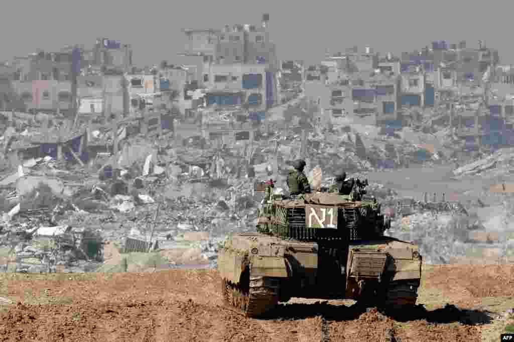 A picture taken from a position in southern Israel shows an Israeli tank rolling along the fence as damaged buildings are see in the Gaza Strip.