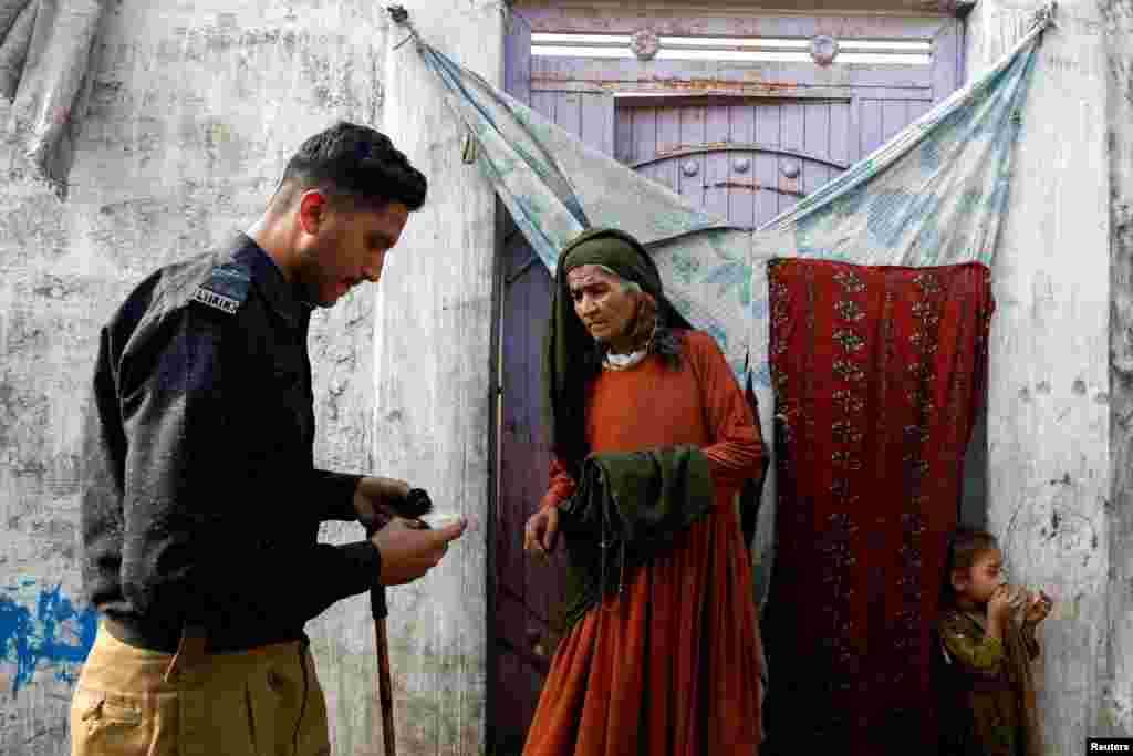A police officer checks the registration card of Edema Bibi, 66, an Afghan citizen, outside her house in an Afghan Camp on the outskirts of Karachi, Pakistan, during a door-to-door search and verification drive for undocumented Afghan nationals, Nov. 21, 2023.