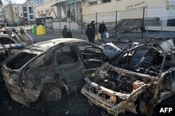 People walk near cars that were destroyed by recent shelling on the outskirts of Kyiv, Feb. 28, 2022. (Photo by Genya SAVILOV / AFP)