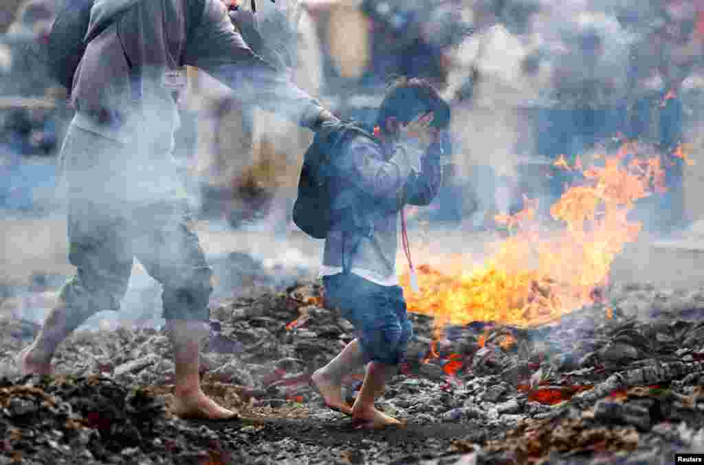 A boy and a man walk next to flames as they walk over coal with barefoot at the fire-walking festival, called Hiwatari Matsuri in Japanese, at Mt.Takao in Tokyo.