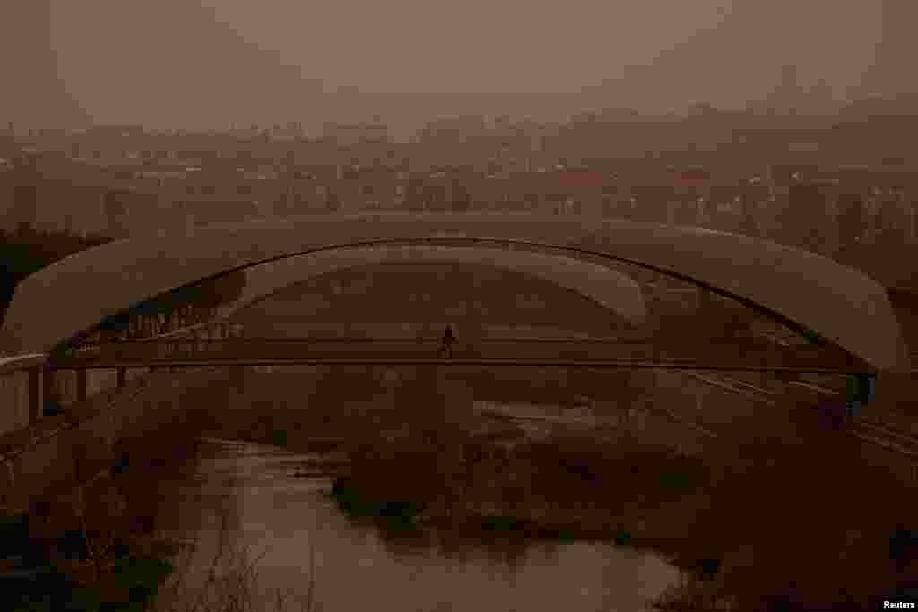 A person wearing a protective mask crosses a bridge as storm Celia blows sand from the Sahara desert over Madrid, Spain.