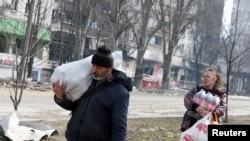 Residentes locales que llevan alimentos pasan frente un edificio de apartamentos dañado por bombardeos rusos en la sitiada ciudad portuaria de Mariupol, en el sur de Ucrania, el 31 de marzo de 2022. REUTERS/Alexander Ermochenko