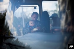 A man feeds a child as they arrive by bus at a reception center for displaced people in Zaporizhzhia, Ukraine, Monday, May 2, 2022. (AP Photo/Francisco Seco)