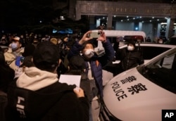 Protesters pass near a police car in Beijing, Sunday, Nov. 27, 2022. (AP Photo/Ng Han Guan)