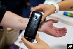 An exhibiter applies a temporary tattoo with a Prinker digital temporary tattoo device during CES Unveiled before the start of the CES tech show, Tuesday, Jan. 3, 2023, in Las Vegas. (AP Photo/John Locher)