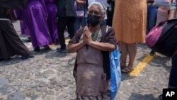 Una mujer de rodillas en oración mientras "Cucuruchos" llevan una estatua de Jesucristo en una carroza religiosa durante una procesión del Jueves Santo, en Antigua, Guatemala, (Foto Moisés Castillo / AP)