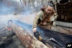 In this Thursday, Nov. 15, 2018, photo, Mashpee Wampanoag Phillip Wynne, of Sagamore, Mass., pours water to control fire and temperatures while making a mishoon, a type of boat, from a tree at the Wampanoag Homesite at Plimoth Plantation, in Plymouth.