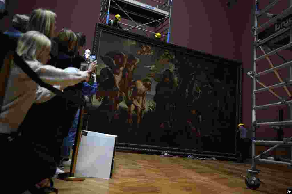 People take photos with their mobile phones as technicians and art handlers move the "Baptism of Christ," by Baroque painter Peter Paul Rubens inside a gallery at the Royal Museum of Fine Arts Antwerp in Antwerp, Belgium.