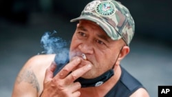 FILE - A man sits while smoking in Auckland, New Zealand, Thursday, Dec. 9, 2021. New Zealand on Tuesday passed into law a unique plan to phase out tobacco smoking by imposing a lifetime ban on young people buying cigarettes. (AP Photo/David Rowland, File)