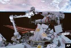 In this photo released by Xinhua News Agency, screen image captured at the Beijing Aerospace Control Center on Sept. 1, 2022 shows Shenzhou-14 astronauts Chen Dong, at top and Liu Yang conducting extravehicular activities out of the space station lab module Wentian orbiting earth. (Li Jie/Xinhua via AP)