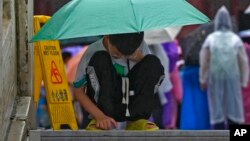 FILE - A boy covering himself with an umbrella from the rain, browses a smartphone placed on the ground at the Forbidden City in Beijing on July 13, 2023. (AP Photo/Andy Wong)