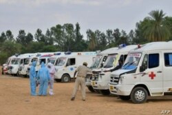 Familiares con equipo de protección aparecen junto a ambulancias que transportan cuerpos de víctimas del COVID, en un lugar de cremación al aire libre instalado en las afueras de Bangalore, India, el 8 de mayo de 2021.
