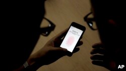 In this Sept. 11, 2013, file photo, an Apple employee, right, instructs a journalist on the use of the fingerprint scanner technology built into the company's iPhone 5S during a media event in Beijing, China. (AP Photo/Ng Han Guan, File)