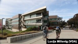 Two students ride bicycles past the Rady School of Management at UC San Diego.