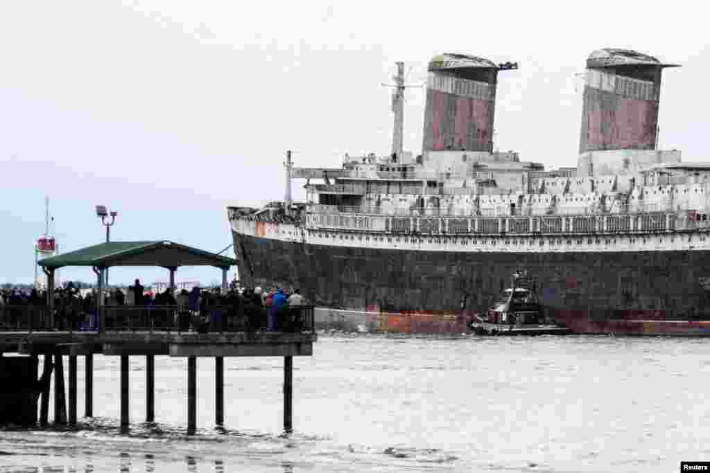 Onlookers watch as SS United States, a retired American ocean liner, is towed out to sea on the Delaware River, on her way to Alabama where she is intended to be sunk to create an artificial reef, in Philadelphia, Pennsylvania, Feb. 19, 2025. The ocean liner was built during 1950 and 1951 for United States Lines. REUTERS/Matthew Hatcher