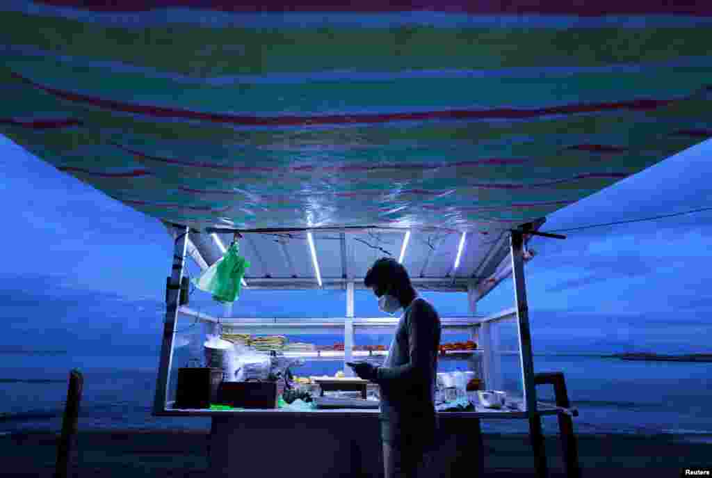 A street vendor wearing a face mask uses his mobile phone while waiting for customers at his food stall near a beach in Colombo, Sri Lanka.