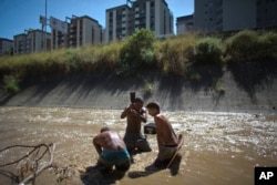 In this Dec. 5, 2017 photo, Angel Villanueva, center, uses a metal bar to break up the mud at the bottom of the polluted Guaire River in Caracas, Venezuela.