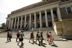 FILE - In this July 16, 2019, file photo people walk past an entrance to Widener Library, behind, on the campus of Harvard University, in Cambridge, Mass.