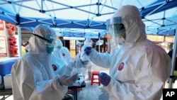 A health official wearing protective gears puts a sample of a person into a plastic bag during the COVID-19 testing at a makeshift clinic in Seoul, South Korea, Friday, June 5, 2020. (AP Photo/Ahn Young-joon)