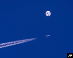 FILE - In this photo provided by Chad Fish, a large balloon drifts above the Atlantic Ocean, just off the coast of South Carolina, with a fighter jet and its contrail seen below it, Saturday, Feb. 4, 2023. The balloon was struck by a missile from an F-22 fighter just off Myrtle Beach, fascinating sky-watchers across a populous area known as the Grand Strand for its miles of beaches that draw retirees and vacationers. (Chad Fish via AP)