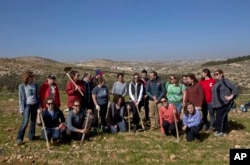 In this Friday, Jan. 25, 2019 photo, American rabbinical students take a group photo, with the village of Attuwani in the background, during a day planting olive trees, near Hebron in the West Bank. (AP Photo/Nasser Nasser)