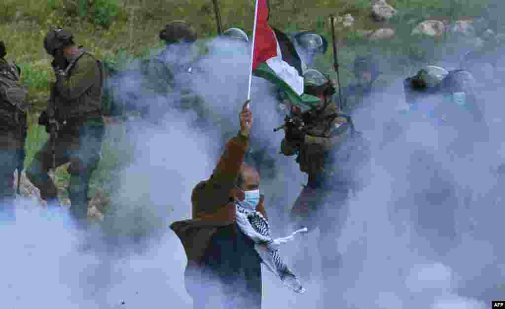 A Palestinian protester raises a national flag as a member of the Israeli forces points his gun, amid smoke from tear gas, during a demonstration against the establishment of Israeli outposts on their lands, in Beit Dajan, in the occupied West Bank.