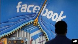FILE - A Facebook employee walks past a sign at Facebook headquarters in Menlo Park, California in 2013.