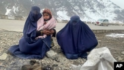Gulnaz, left, keeps her 18-month-old son warm themselves as they wait for alms in the Kabul - Pul-e-Alam highway eastern Afghanistan, Tuesday, Jan. 18, 2022. (AP Photo/Kathy Gannon)