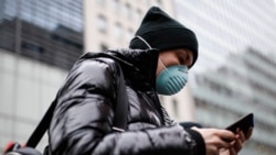 In this file photo, a pedestrian uses her phone while wearing a face mask in Herald Square, Thursday, March 12, 2020, in New York. (AP Photo/John Minchillo)