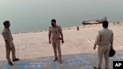Esta imagen de un vídeo proporcionado por KK Productions muestra a oficiales de policía parados en la orilla de un río donde se encontraron varios cuerpos flotando, en el distrito de Ghazipur , Estado de Uttar Pradesh, la India, el 11 de mayo de 2021.