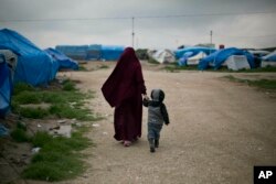 In this March 27, 2019, photo, Samira from Belgium walks with her son at Camp Roj in north Syria. (AP Photo/Maya Alleruzzo)