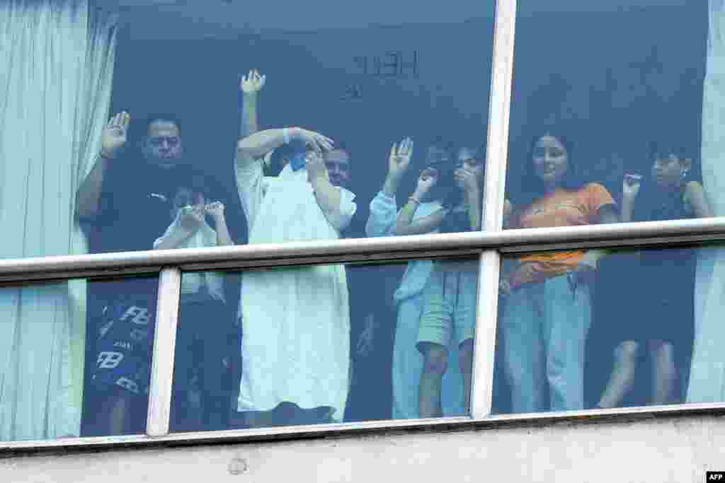 Migrants deported from the U.S. gesture as they look out the window of the Decapolis Hotel where they are temporarily staying in Panama City, on February 18, 2024. Panama's government denied that migrants deported by the United States who were seen holding up signs to hotel windows pleading for help were being held against their will.