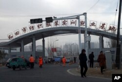 In this Wednesday, Dec. 5, 2018, photo, residents pass by the entrance to the "Hotan City apparel employment training base" where Hetian Taida has a factory in Hotan in western China's Xinjiang region. (AP Photo/Ng Han Guan)