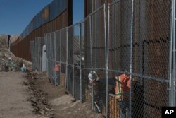 Workers continue work raising a taller fence in the Mexico-US border separating the towns of Anapra, Mexico and Sunland Park, New Mexico, with funding from a 2006 law.