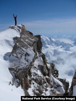 A mountaineer stands atop a tall peak in Denali National Park
