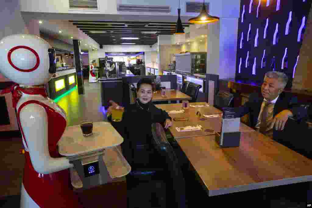 Owners Shu Lei Hu, left, and her husband Shao Song Hu, right, demonstrate the use of robots for serving purposes or for dirty dishes collection at the family's Royal Palace restaurant in Renesse, south-western Netherlands, Wednesday, May 27, 2020. (AP Pho
