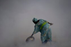 Ndeye Yacine Dieng drops embers over peanut shells covering fish as she walks amidst the smoke on Bargny beach, some 35 kilometers (22 miles) east of Dakar, Senegal, Wednesday April 21, 2021.
