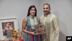 Sheetal Deo and her husband, Sanmeet Deo, hold a Hindu swastika symbol in their home in Syosset, N.Y., on Sunday, Nov. 13, 2022. (AP Photo/Andres Kudacki)