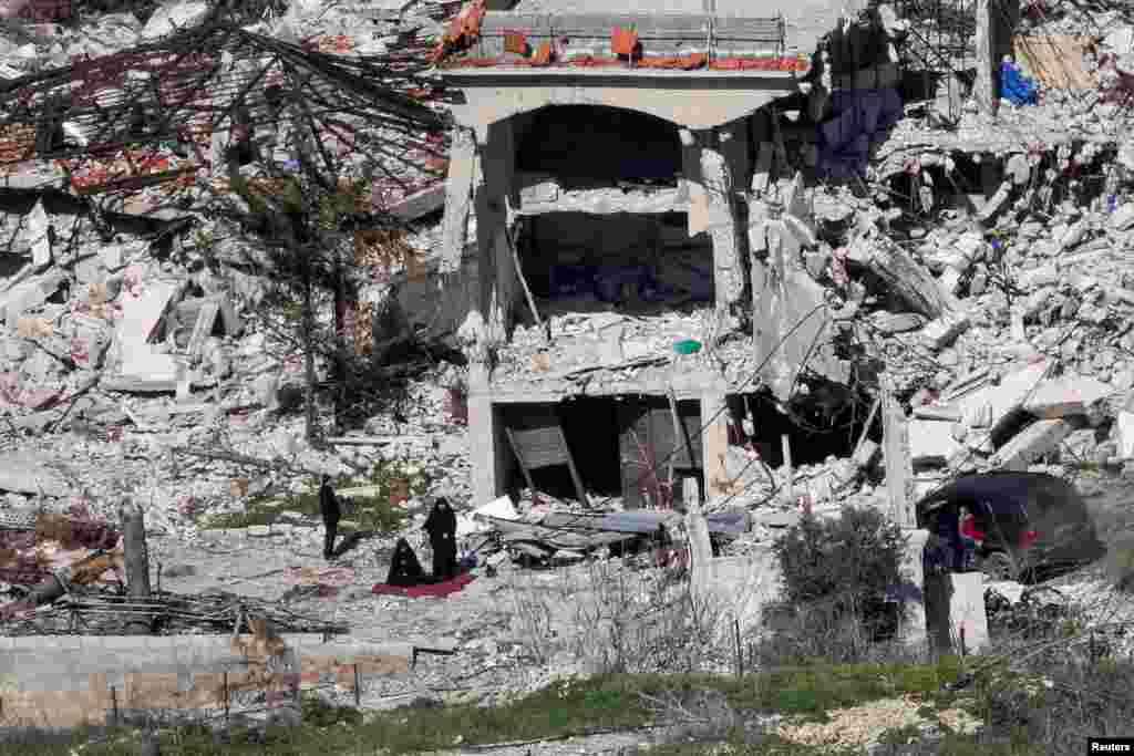 Women pray next to the wreckage of destroyed houses, on the Lebanese side of the Israel-Lebanon border near the village of Adaisseh, as seen from the Israeli.