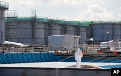FILE - a worker, wearing protective suits and masks, takes notes in front of storage tanks for radioactive water at the tsunami-crippled Fukushima Dai-ichi nuclear power plant, operated by Tokyo Electric Power Co. (TEPCO), in Okuma, Fukushima Prefecture,